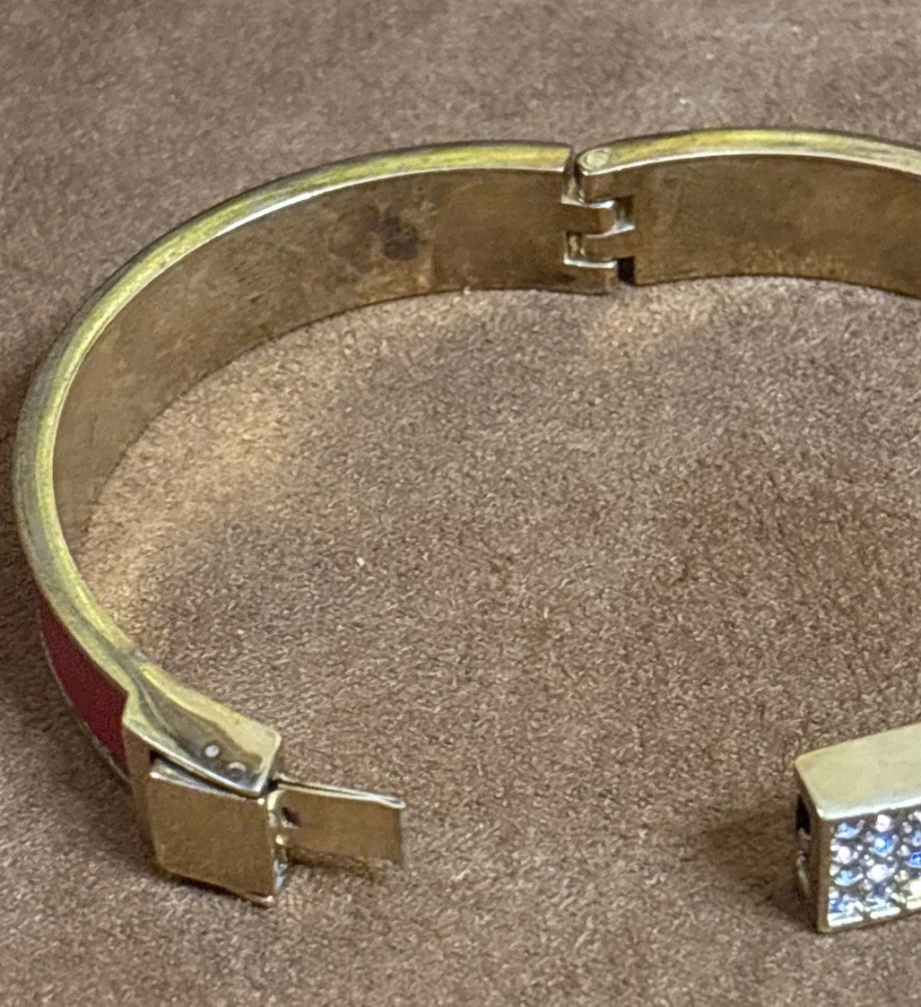 Henri Bendel red leather bangle features a gold-tone metal bar set rhinestones.