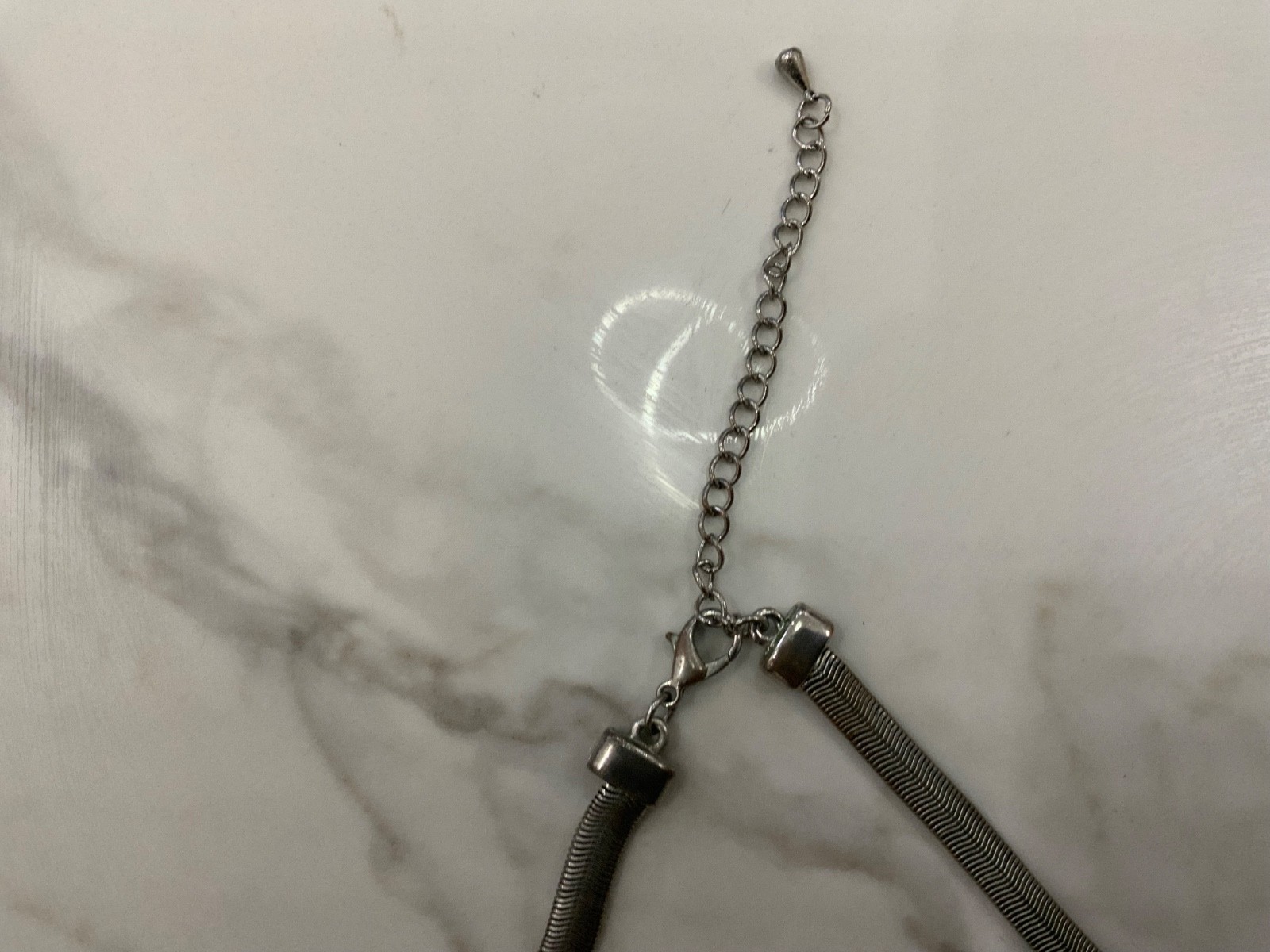 This piece features a flat silver snake chain and a prominent geometric pendant.