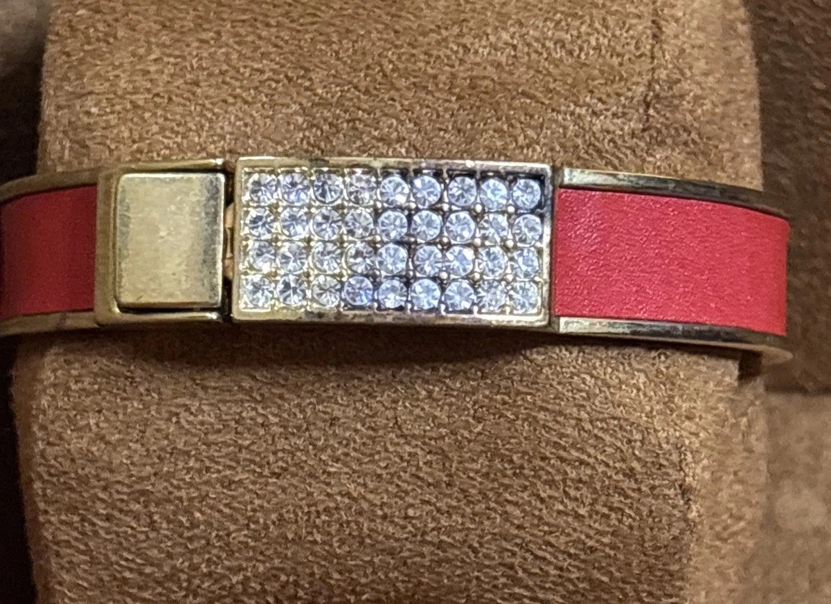 Henri Bendel red leather bangle features a gold-tone metal bar set rhinestones.