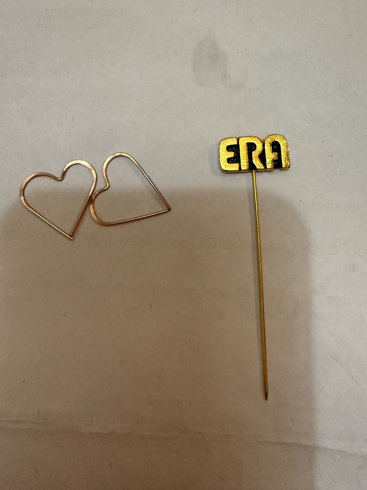 gold-tone “ERA” stick pin, a type of decorative accessory typically worn on lape