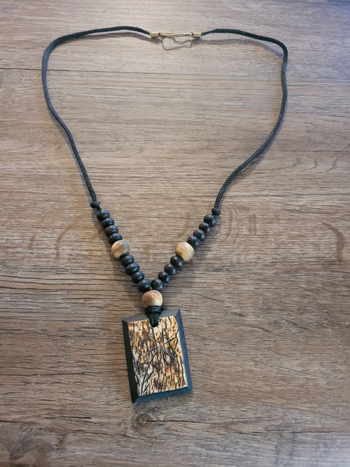 handmade artisan necklace pendant with a textured wood grain finish on a Cord