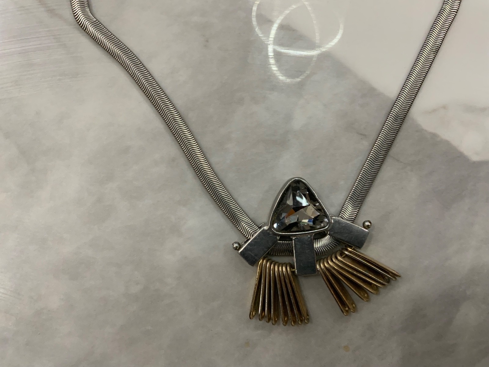 This piece features a flat silver snake chain and a prominent geometric pendant.