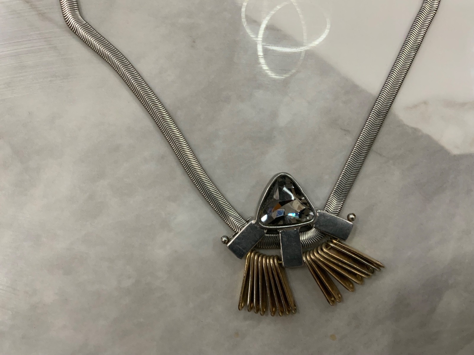 This piece features a flat silver snake chain and a prominent geometric pendant.